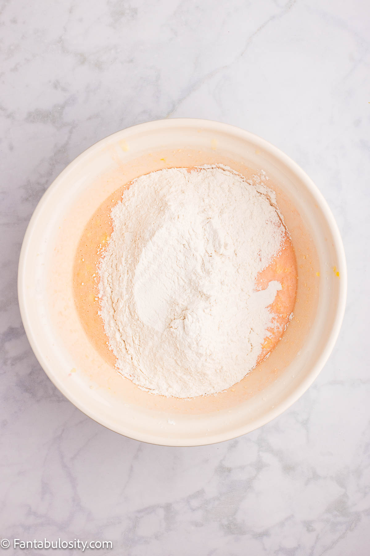 Flour mixture added to cake batter in mixing bowl for cherry cake recipe.