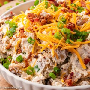 Roasted potato salad in serving bowl, topped with cheese, bacon and green onions.