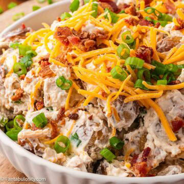 Roasted potato salad in serving bowl, topped with cheese, bacon and green onions.