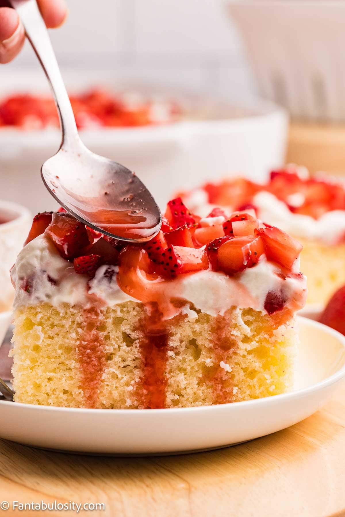 Strawberry drizzle being spooned over the top of a slice of strawberry shortcake.