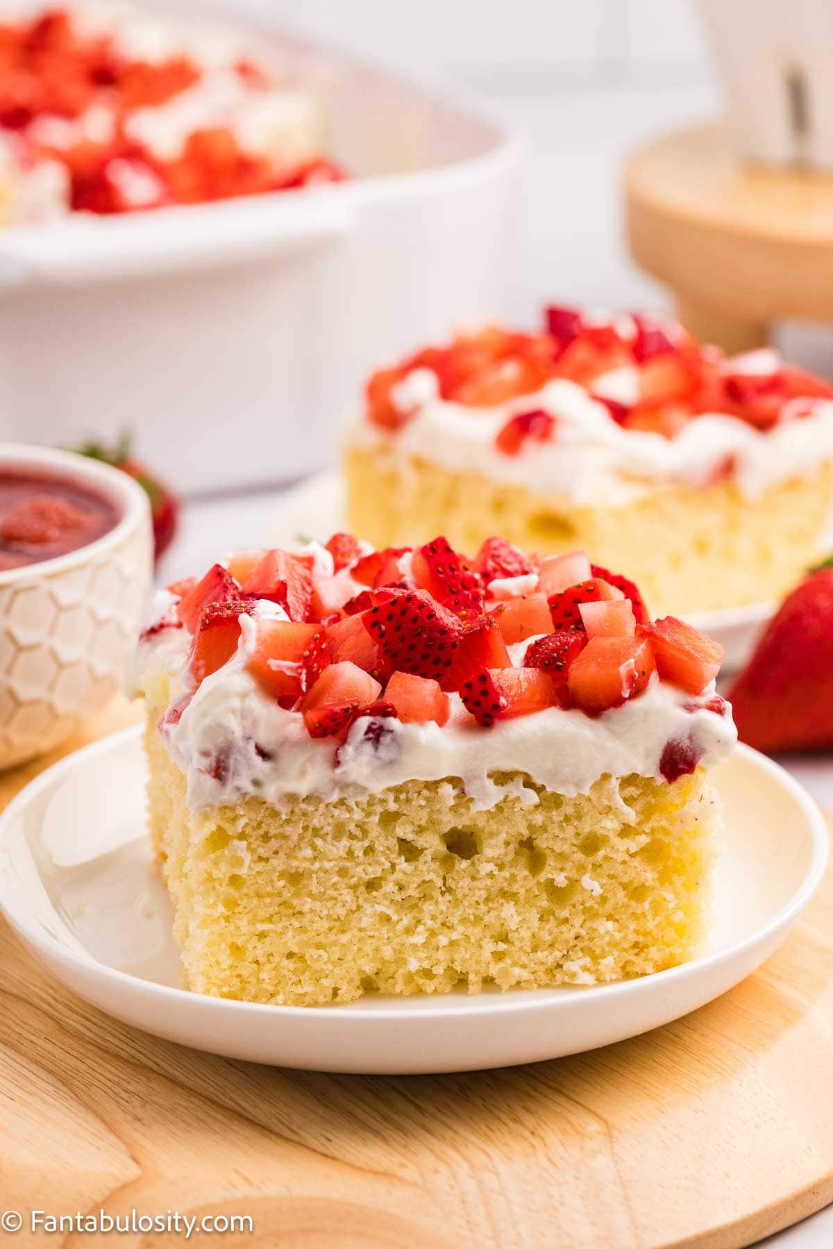 A slice of strawberry shortcake sheet cake sitting on a round plate.