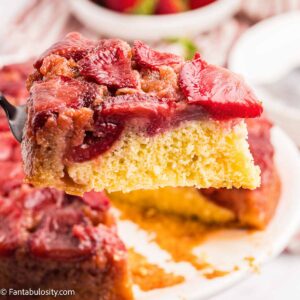 A slice of strawberry upside down cake, being held above round cake.