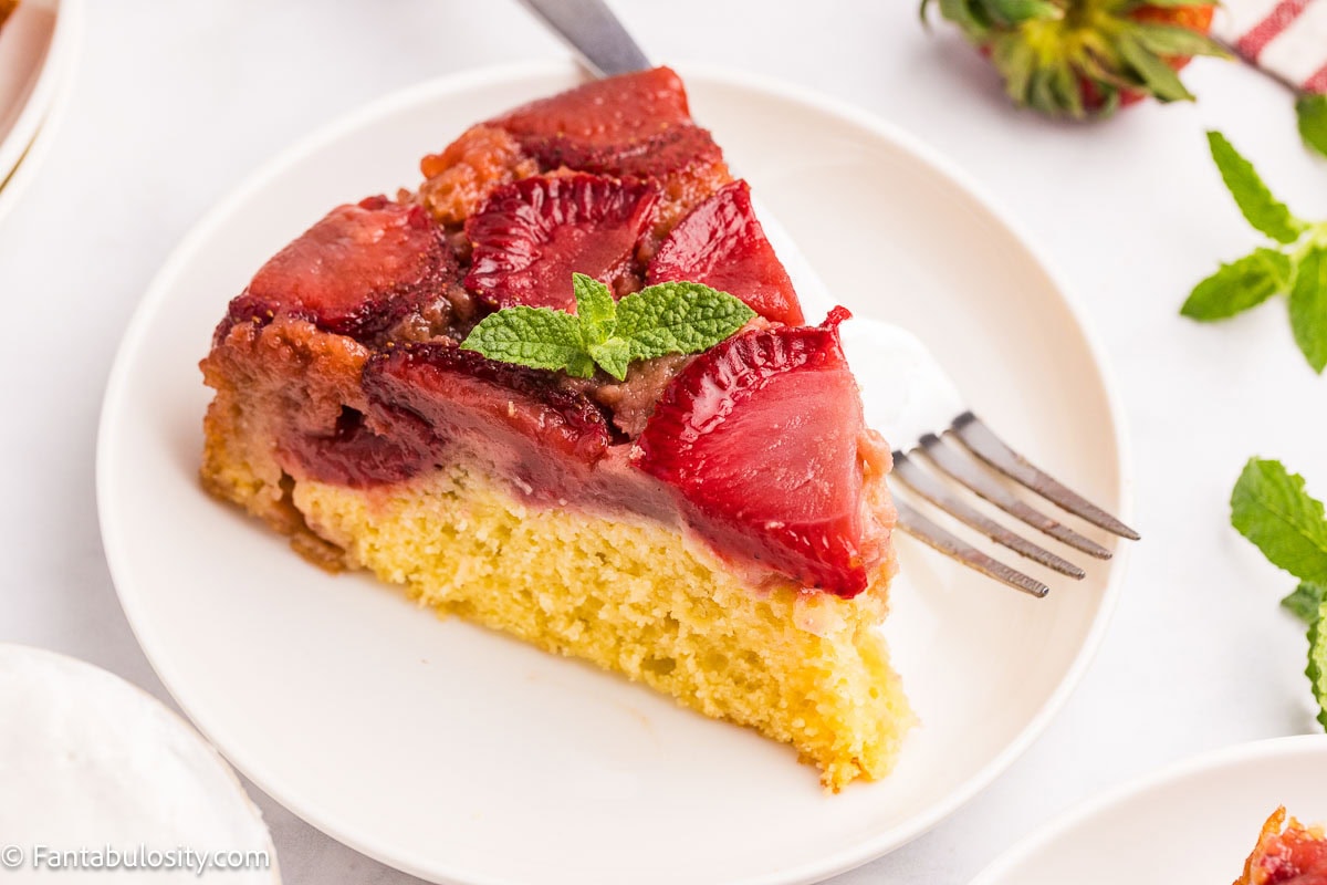A slice of strawberry upside down cake on a round plate with a fork.