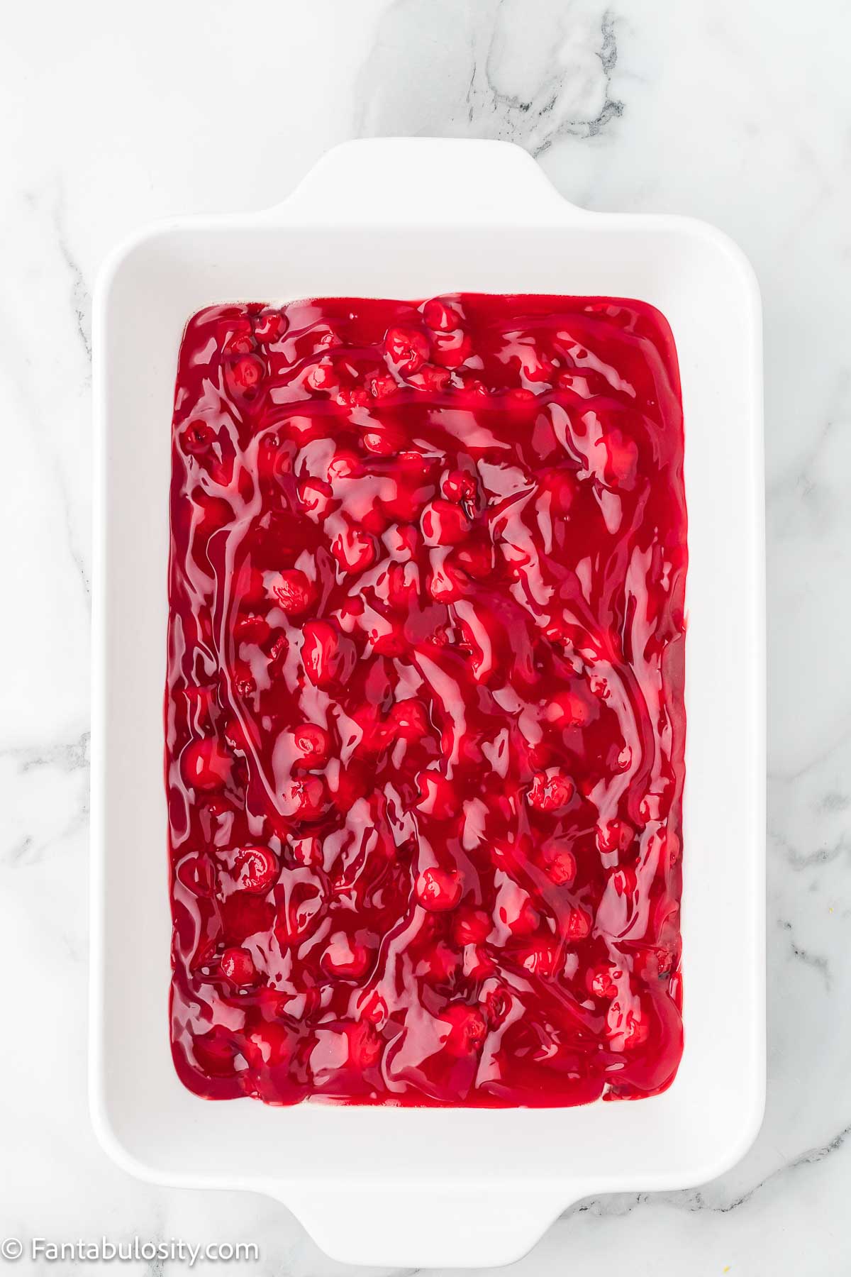 Cherry pie filling spread out in 9x13 baking dish for cherry cheesecake dump cake.