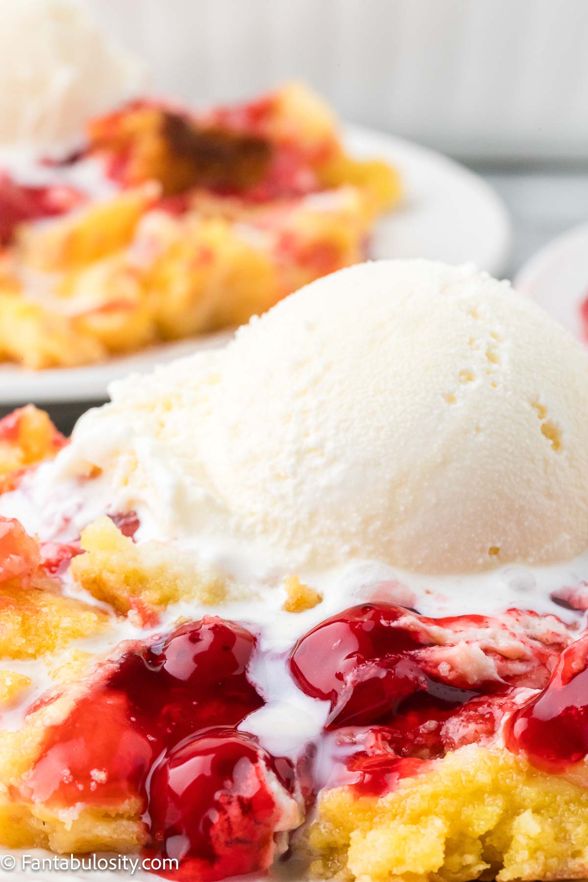 Cherry cheesecake dump cake on a plate, topped with vanilla ice cream.