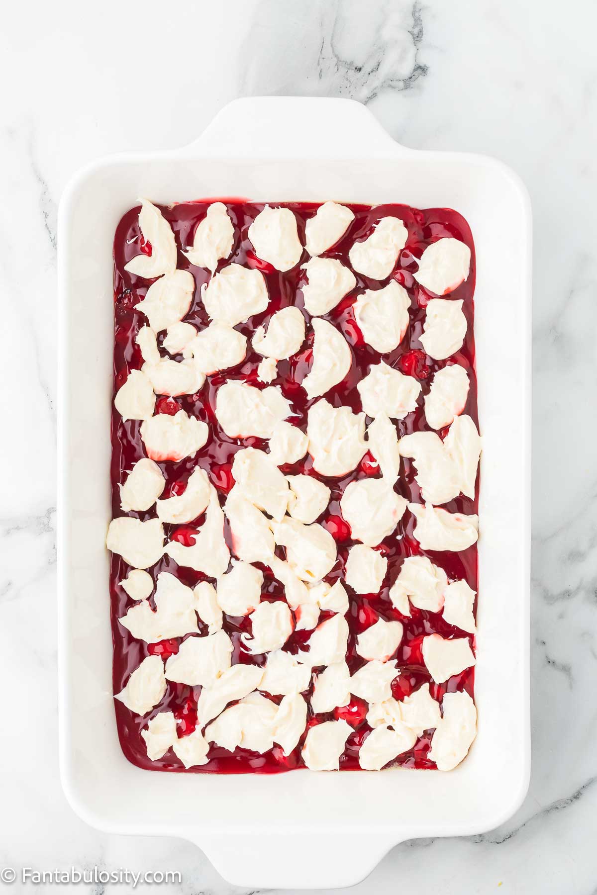 Cream cheese dolloped on to cherry pie filling for dump cake.