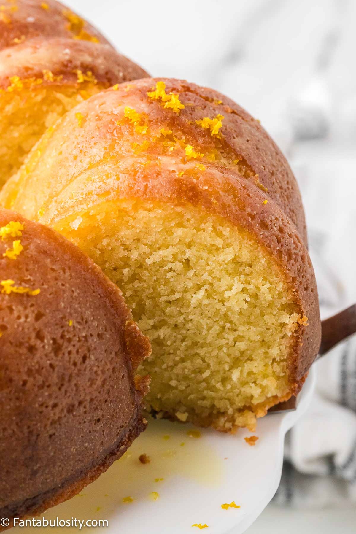 Orange juice cake sliced on cake plate, showing zest and inside of cake.