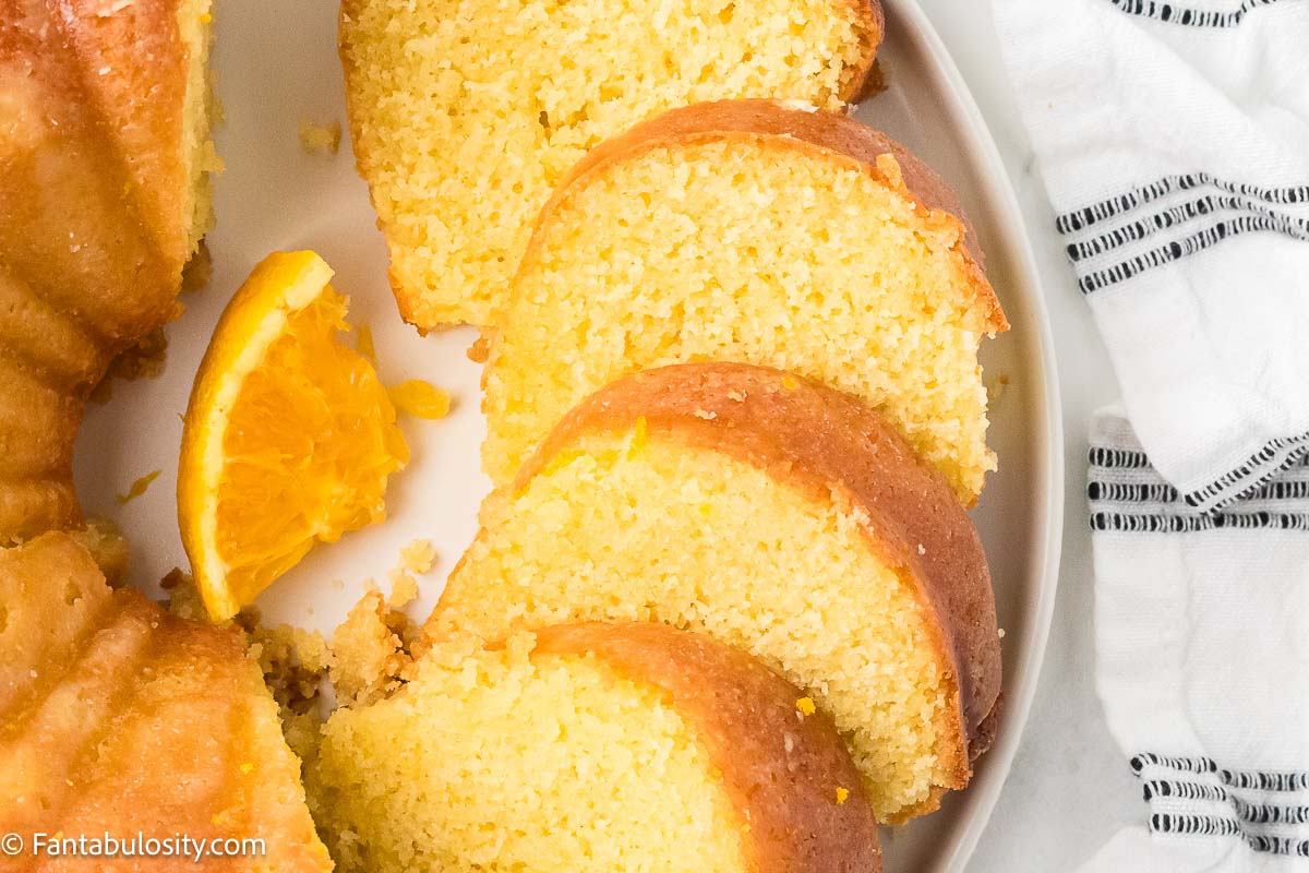 Sliced orange juice cake, on a plate, next to a black and white tea towel.