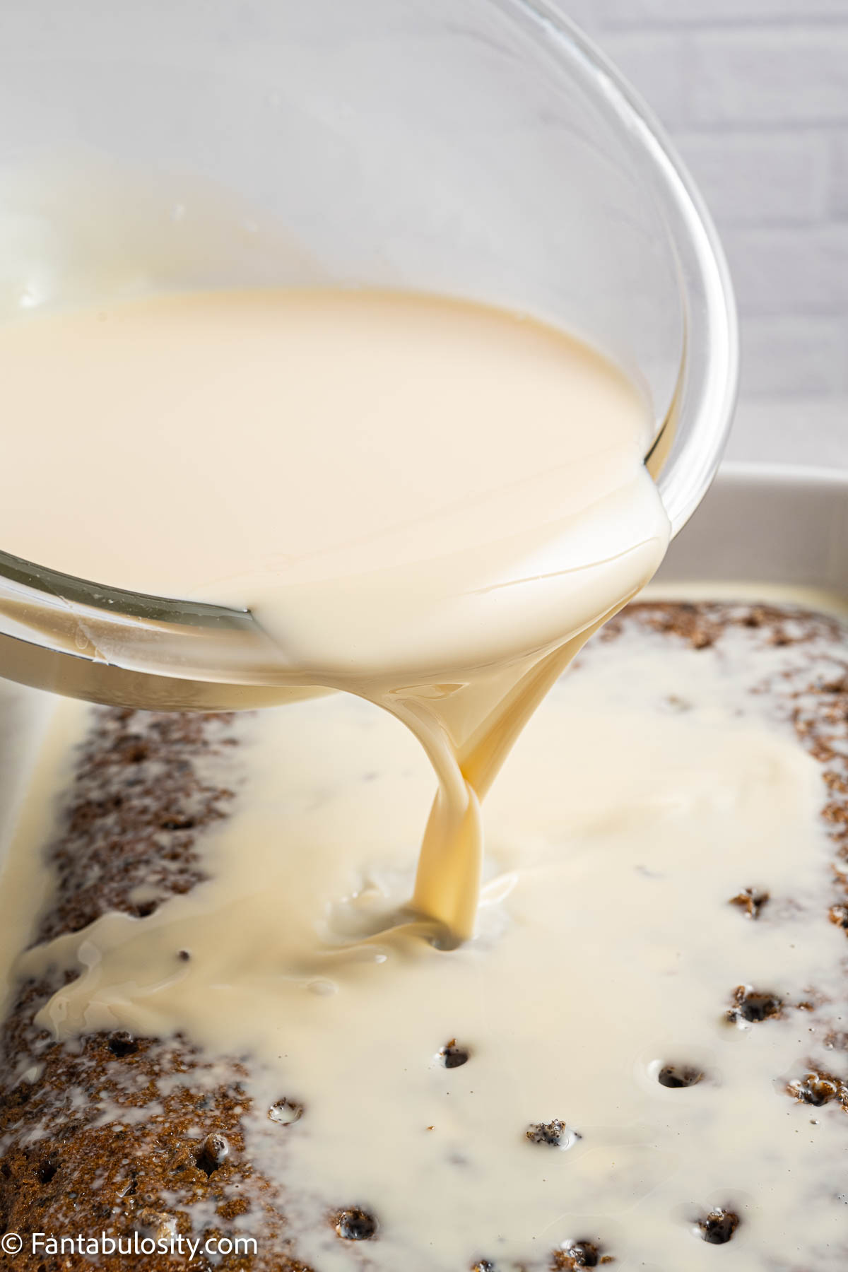 Milk mixture pouring over poked cake.