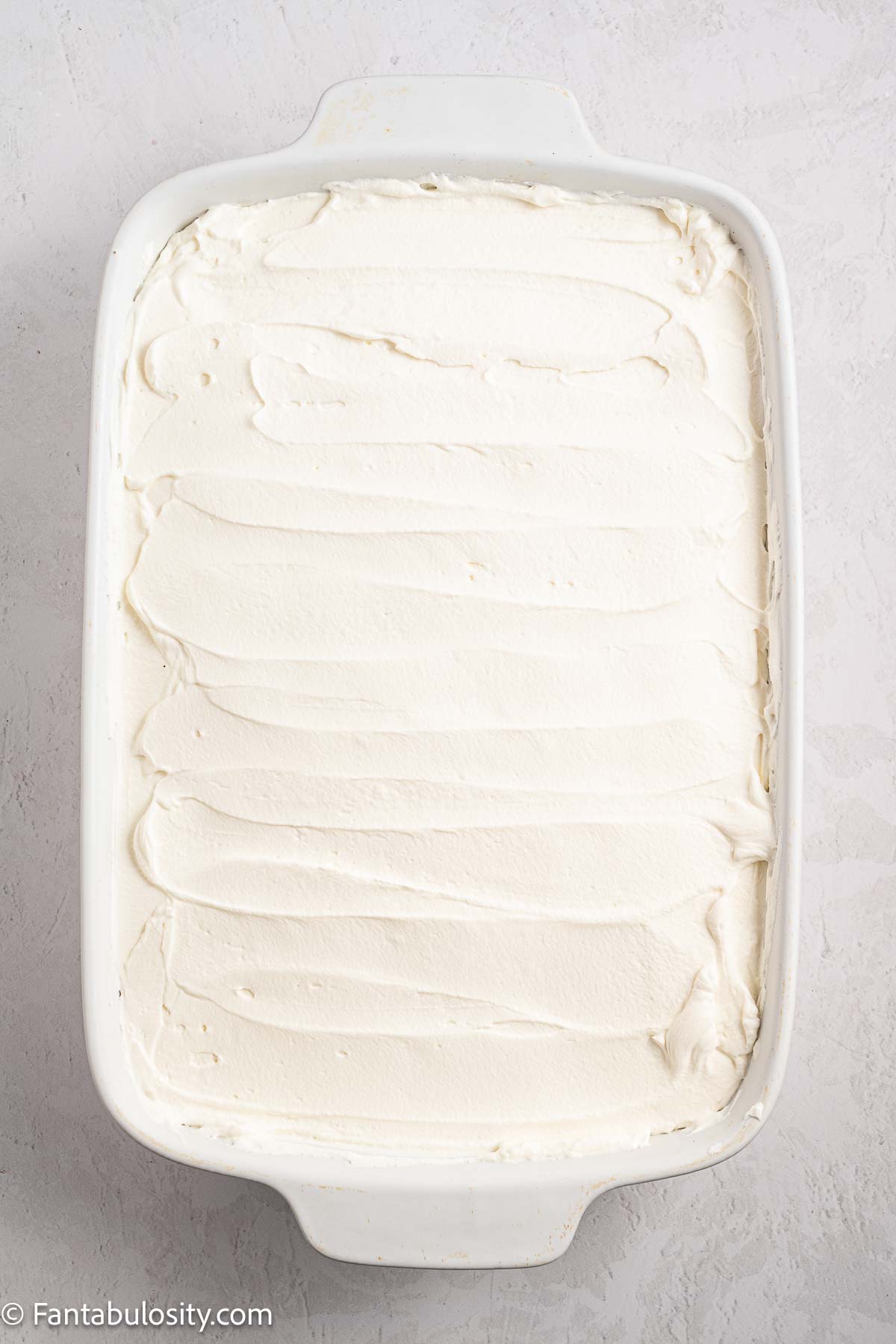 Frosting spread on top of Oreo Tres Leches cake in 9x13 baking pan.