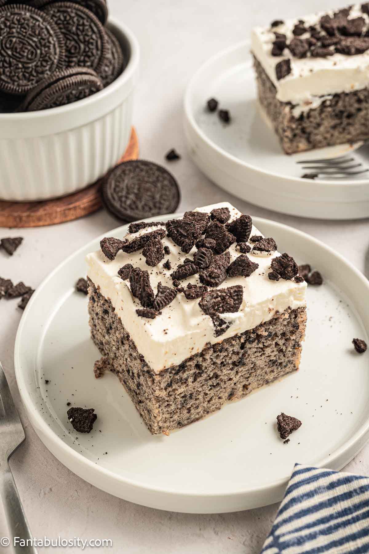 A slice of Oreo Tres Leches cake on a plate, next to a bowl of Oreos.