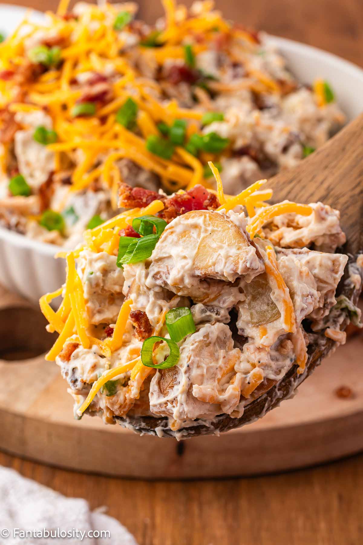 A wooden spoon dishing out a serving of roasted potato salad. 