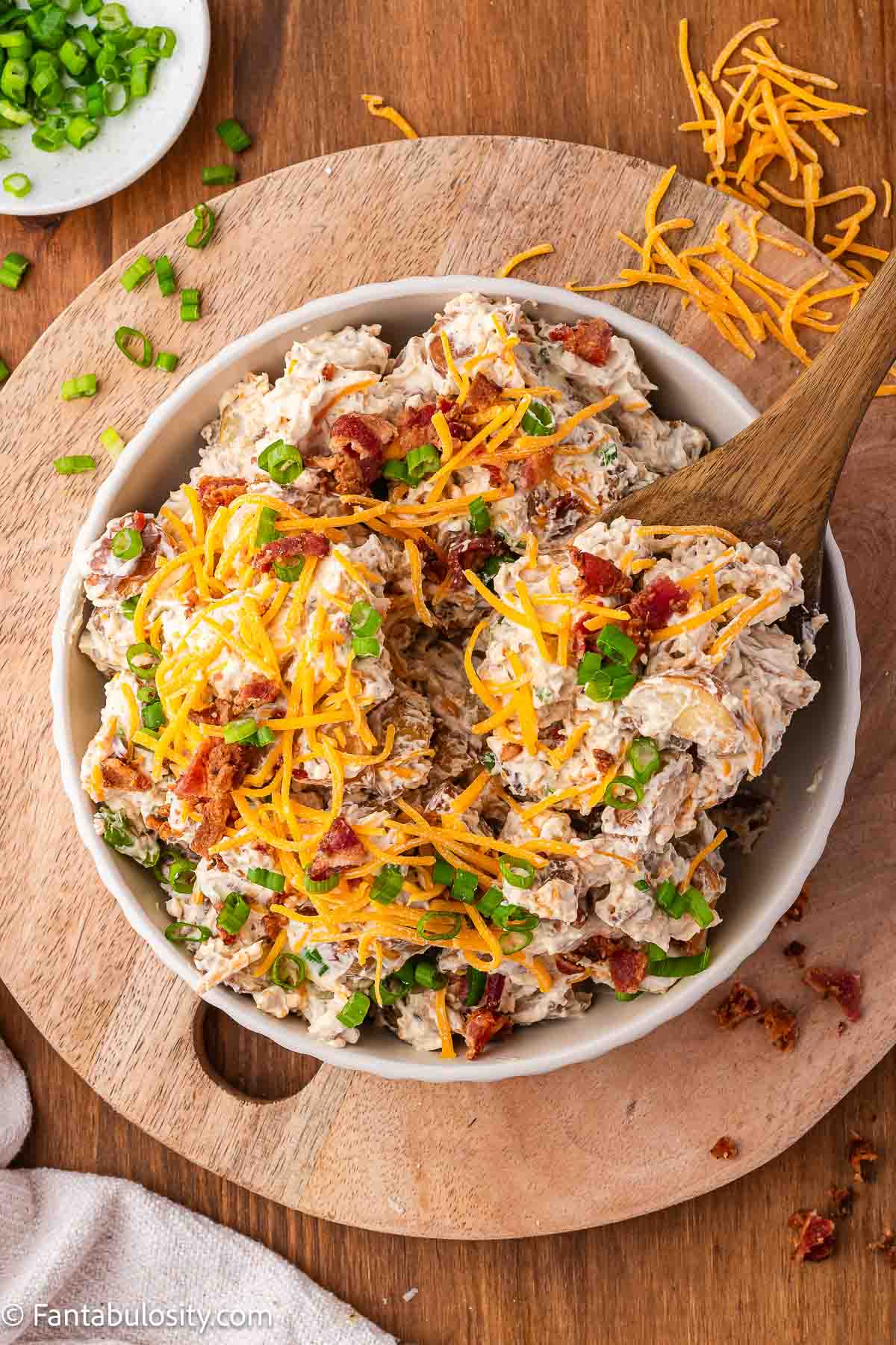 Roasted potato salad in mixing bowl, topped with cheese and green onions.