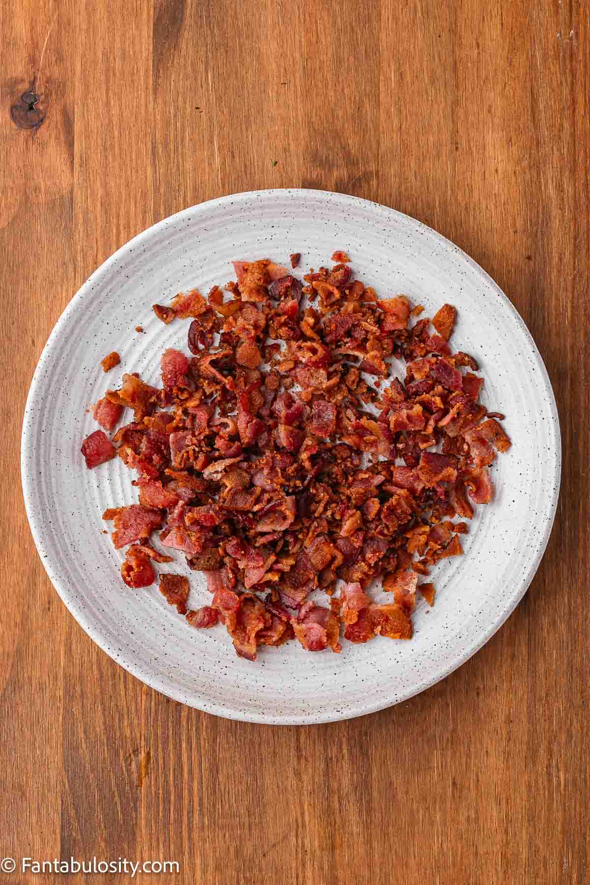 Cooked bacon cut in to pieces and resting on a plate.