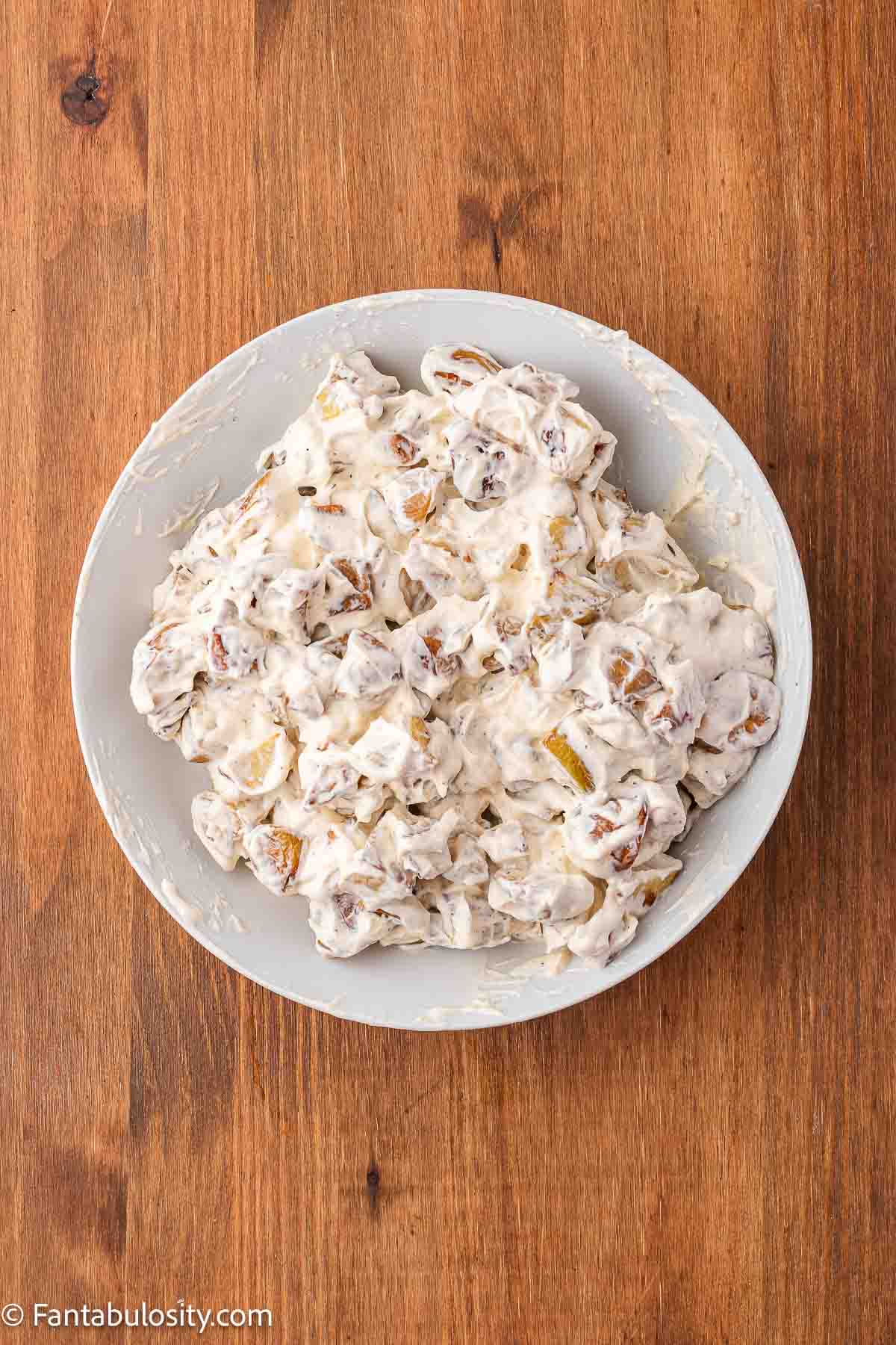 Roasted potatoes mixed with dressing in mixing bowl.