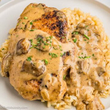 Smothered pork chop with mushroom gravy on top of rice in a plate.