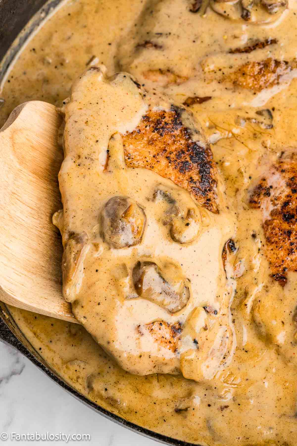 Smothered pork chop on a wooden spatula, out of skillet.
