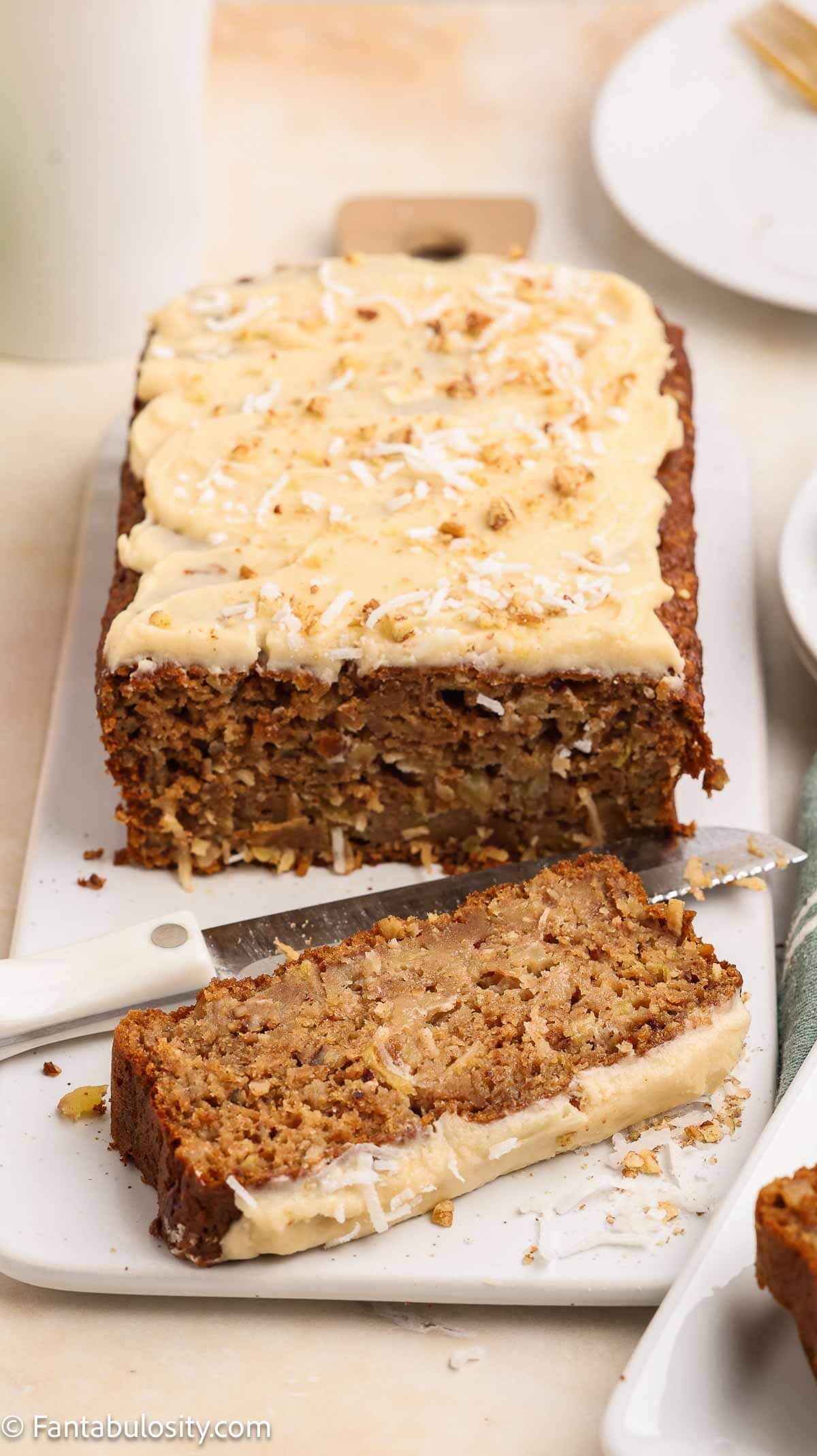 Loaf of apple bread with maple glaze and a slice lying in front.