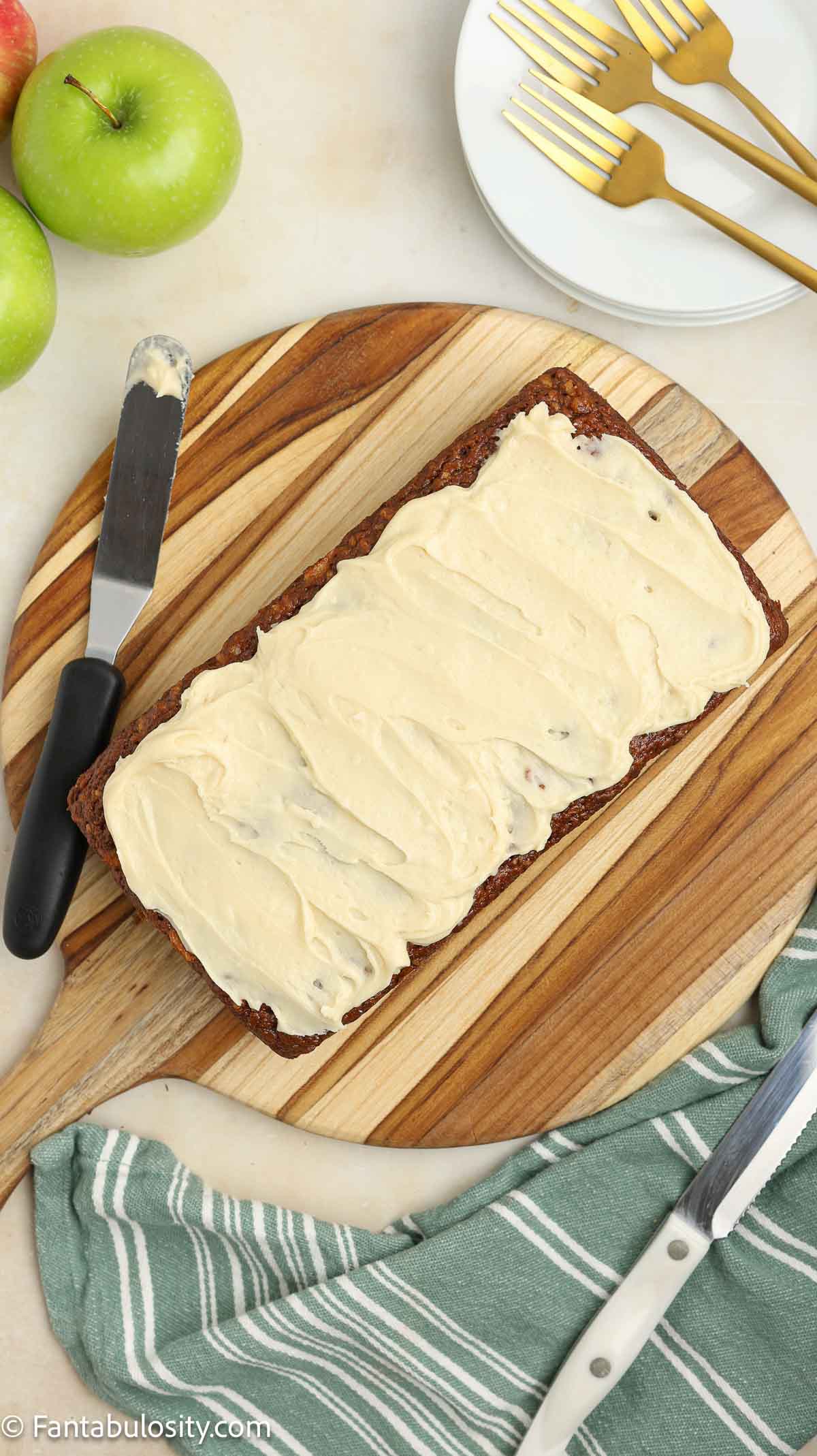 Maple glaze spread on top of apple bread, sitting on wooden cutting board.