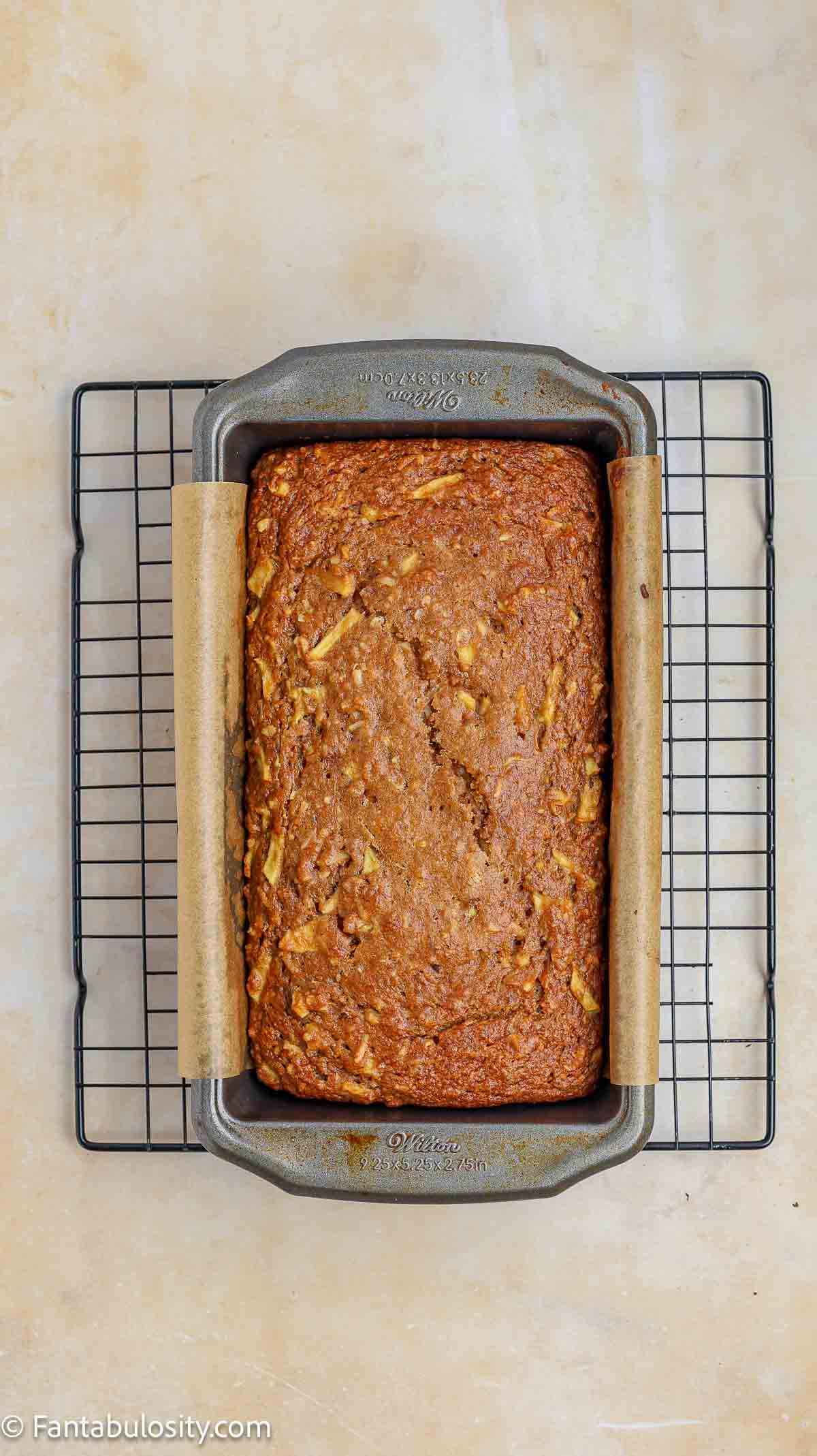 Baked apple bread in loaf pan on wire cooling rack.