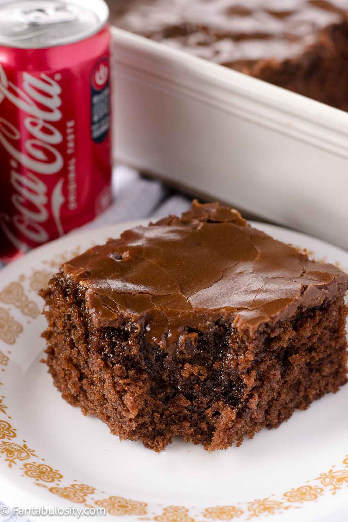 A slice of Coca-Cola Cake on a vintage plate, sitting next to a can of Coke.