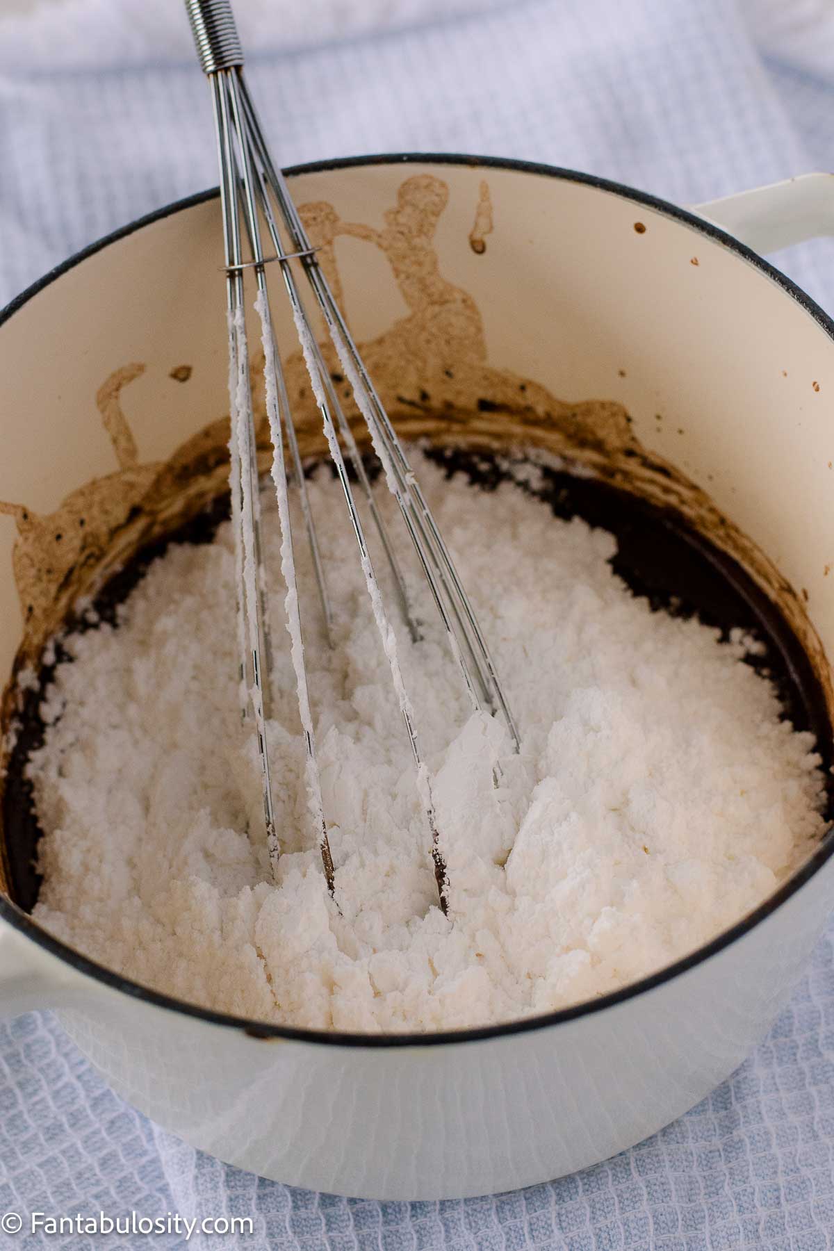 Powdered sugar added to sauce pan with chocolate frosting mixture.