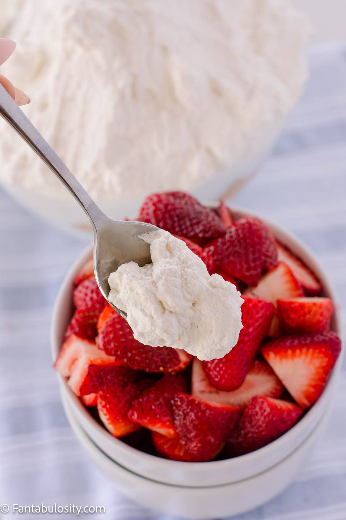 Spoon holding a bite of homemade whipped cream over a bowl of strawberries.