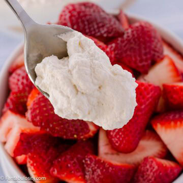 Spoonful of homemade whipped cream with a bowl of strawberries.