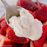 A spoonful of homemade whipped cream resting above strawberries.
