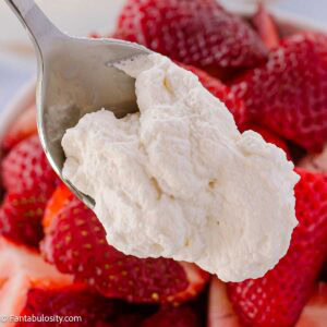 A spoonful of homemade whipped cream resting above strawberries.