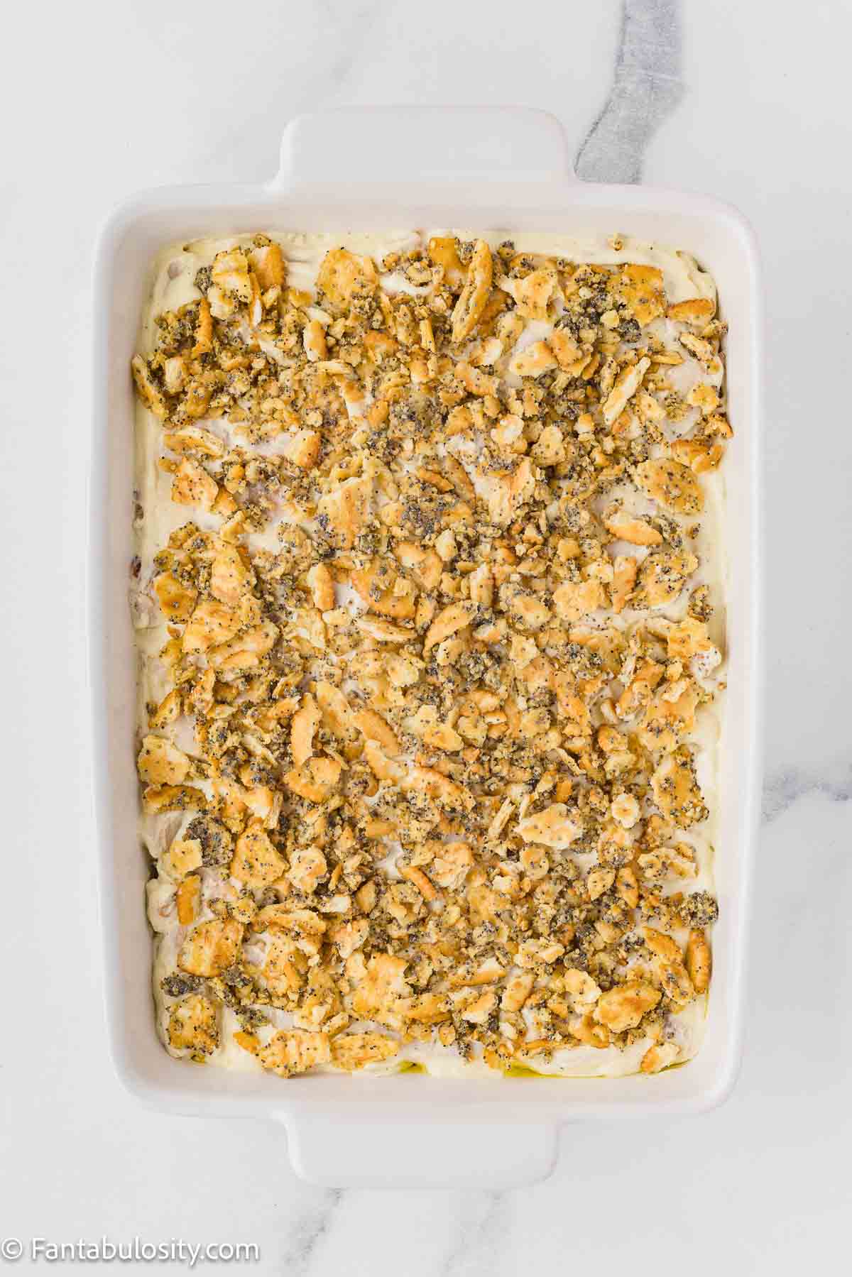 Cracker topping spread on top of poppy seed chicken casserole, ready for baking.