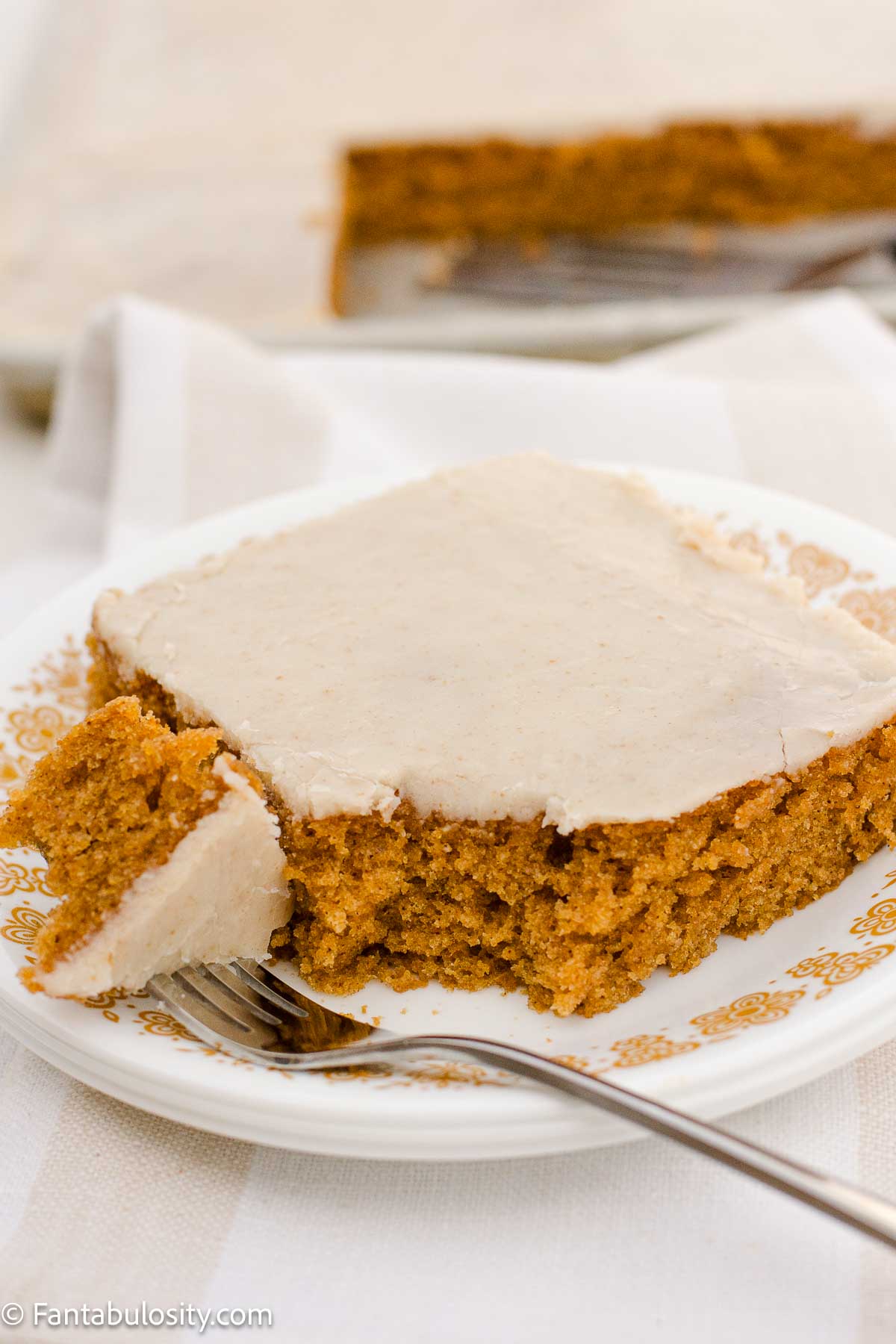 A slice of pumpkin sheet cake with brown butter frosting, and a fork taking a bite.