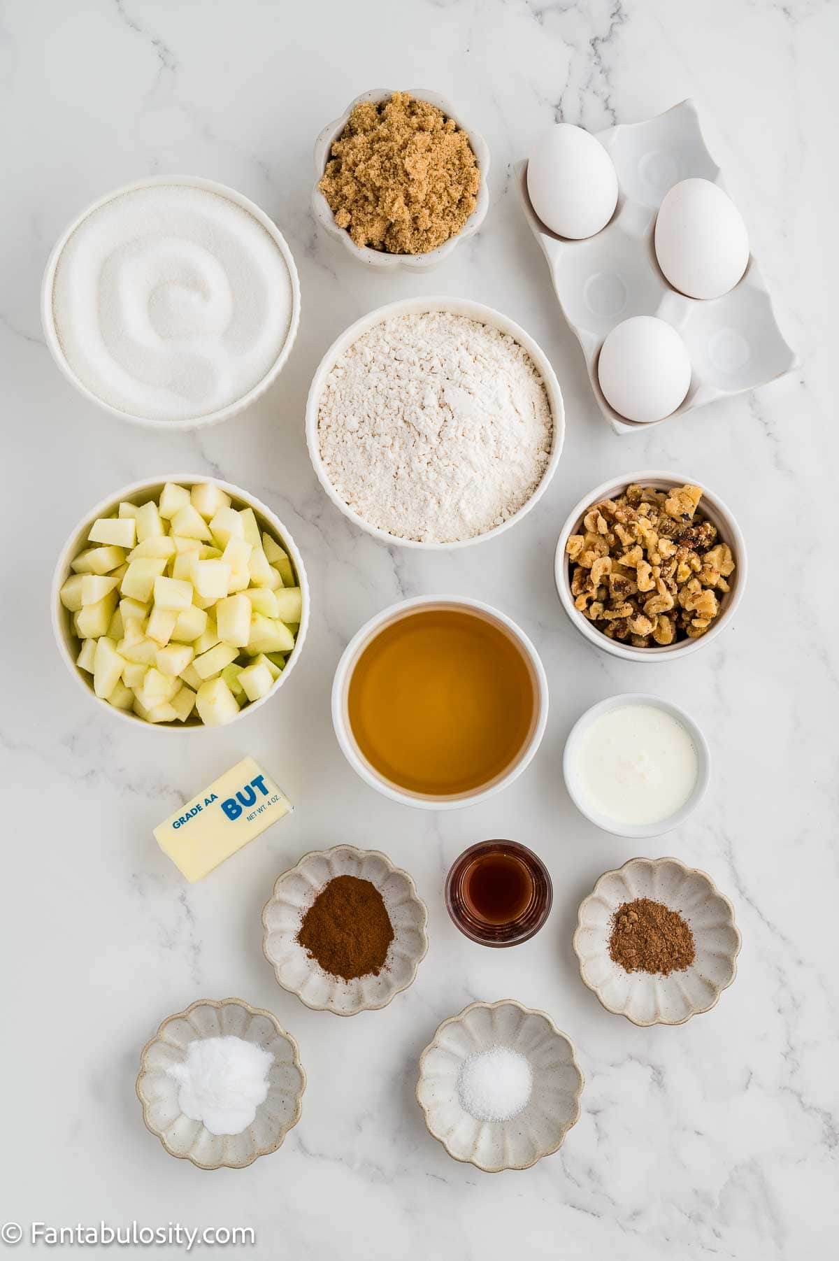 Ingredients for apple dapple cake measured into bowls on a marble counter.