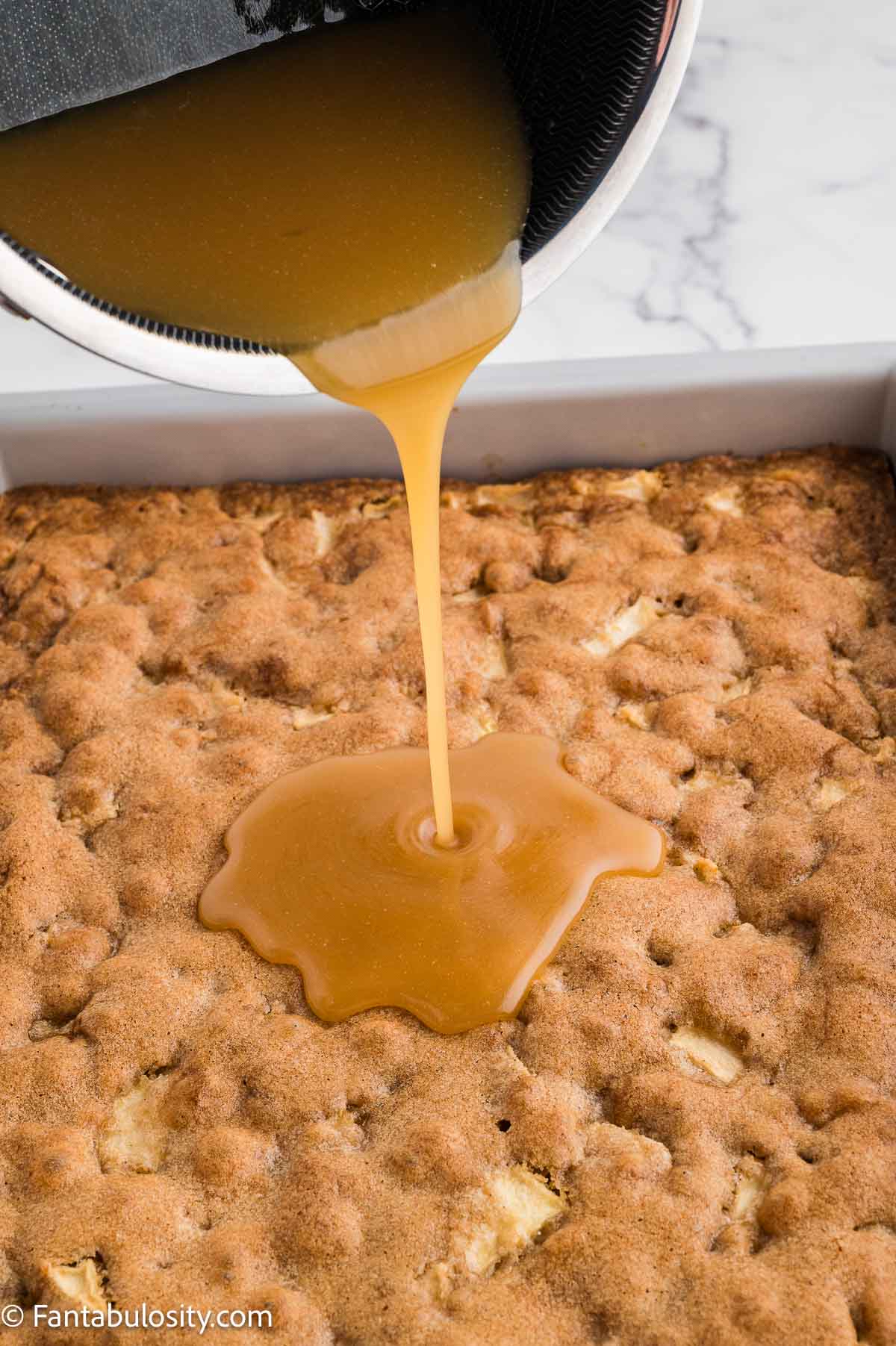 Warm caramel glaze being poured over a pan of apple dapple cake.