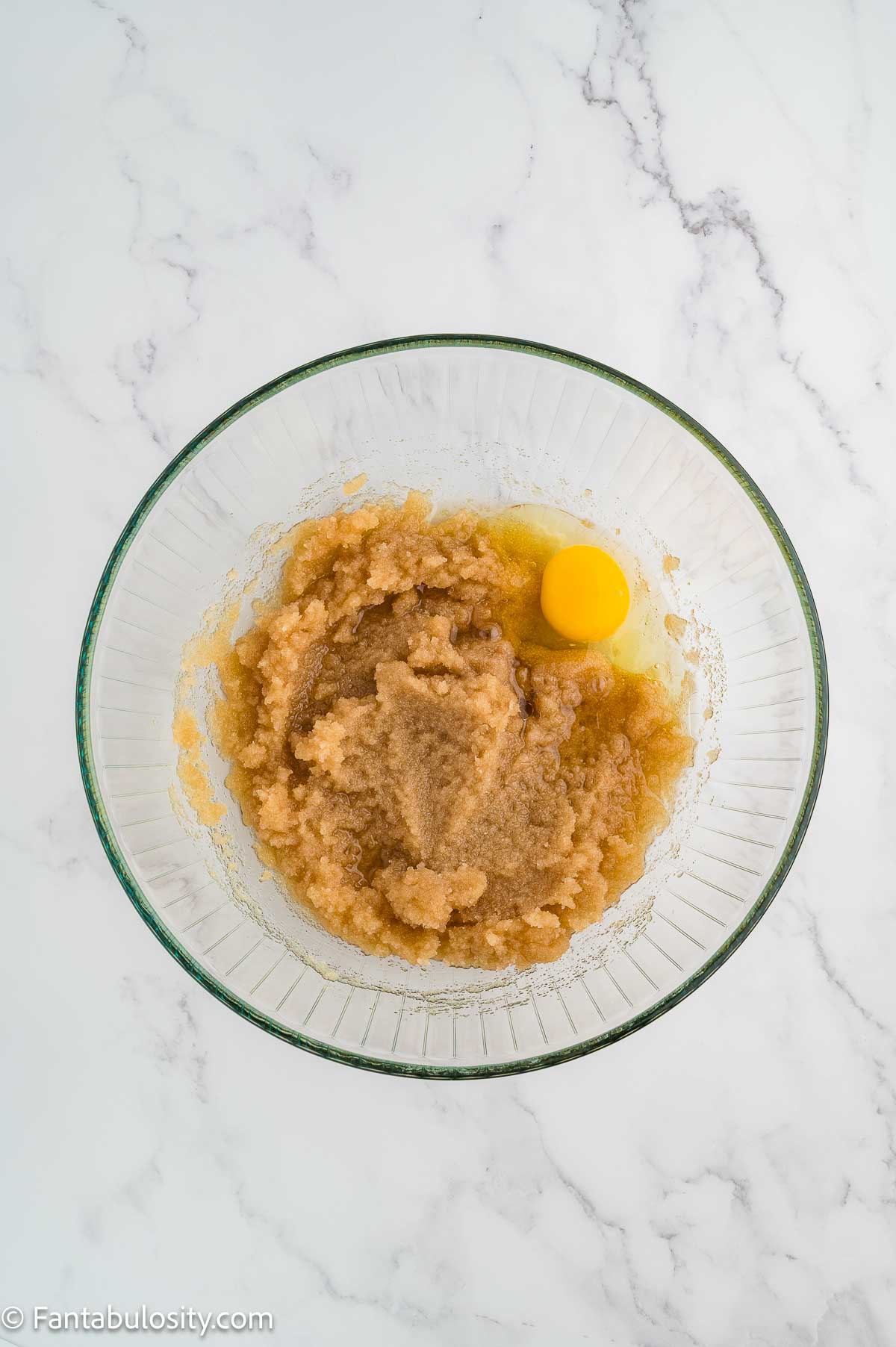 Egg added to sugar and oil mixture in mixing bowl.
