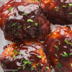 Baked BBQ chicken thighs with crispy skin and a sticky caramelized glaze, sprinkled with parsley.