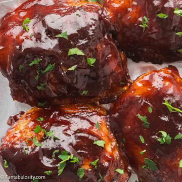 Baked BBQ chicken thighs with crispy skin and a sticky caramelized glaze, sprinkled with parsley.