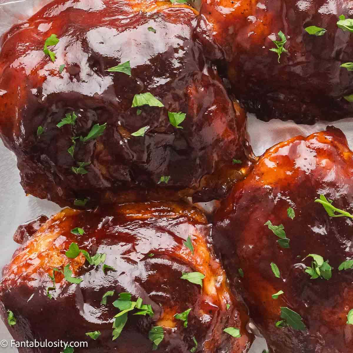Baked BBQ chicken thighs with crispy skin and a sticky caramelized glaze, sprinkled with parsley.