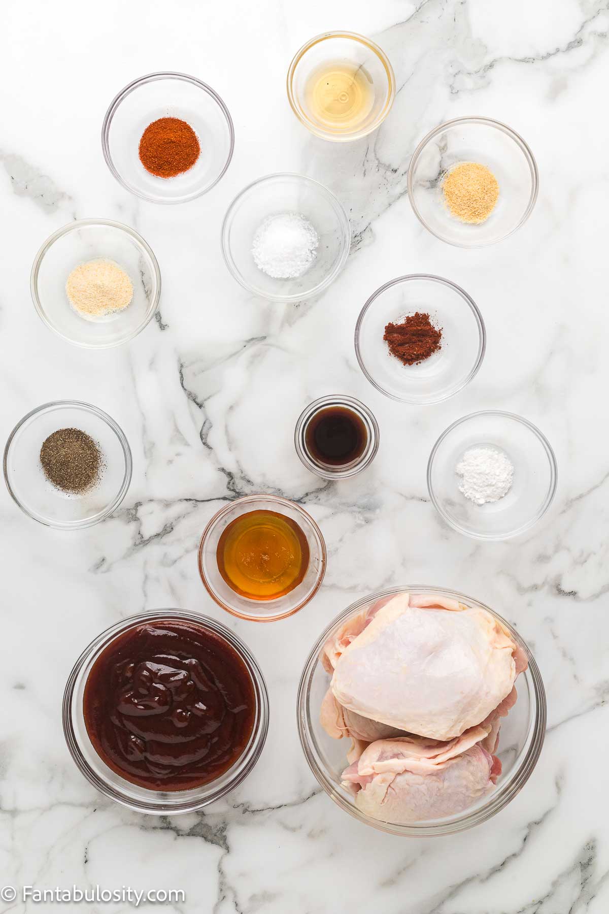 Ingredients for baked BBQ chicken thighs measured into bowls on a marble counter.