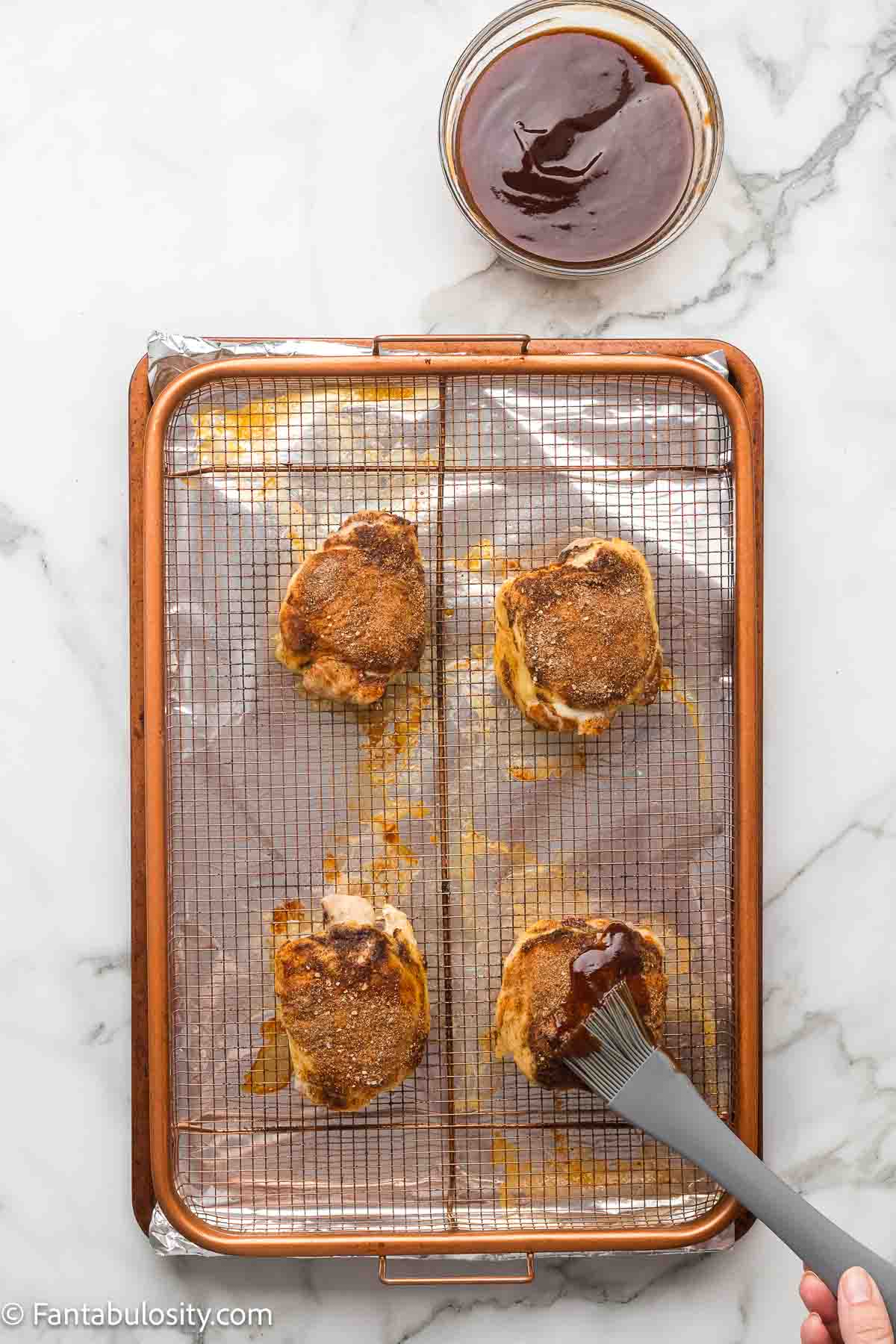 Brushing the first thin layer of BBQ glaze onto baked chicken thighs on a wire rack.
