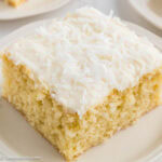 Slice of coconut sheet cake with fluffy coconut frosting on a white plate.