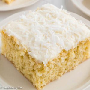 Slice of coconut sheet cake with fluffy coconut frosting on a white plate.