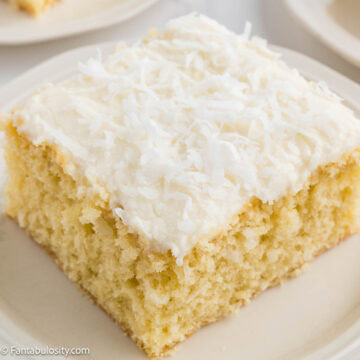Slice of coconut sheet cake with fluffy coconut frosting on a white plate.