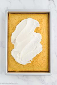 Coconut frosting being spread over the cooled coconut sheet cake in the pan.