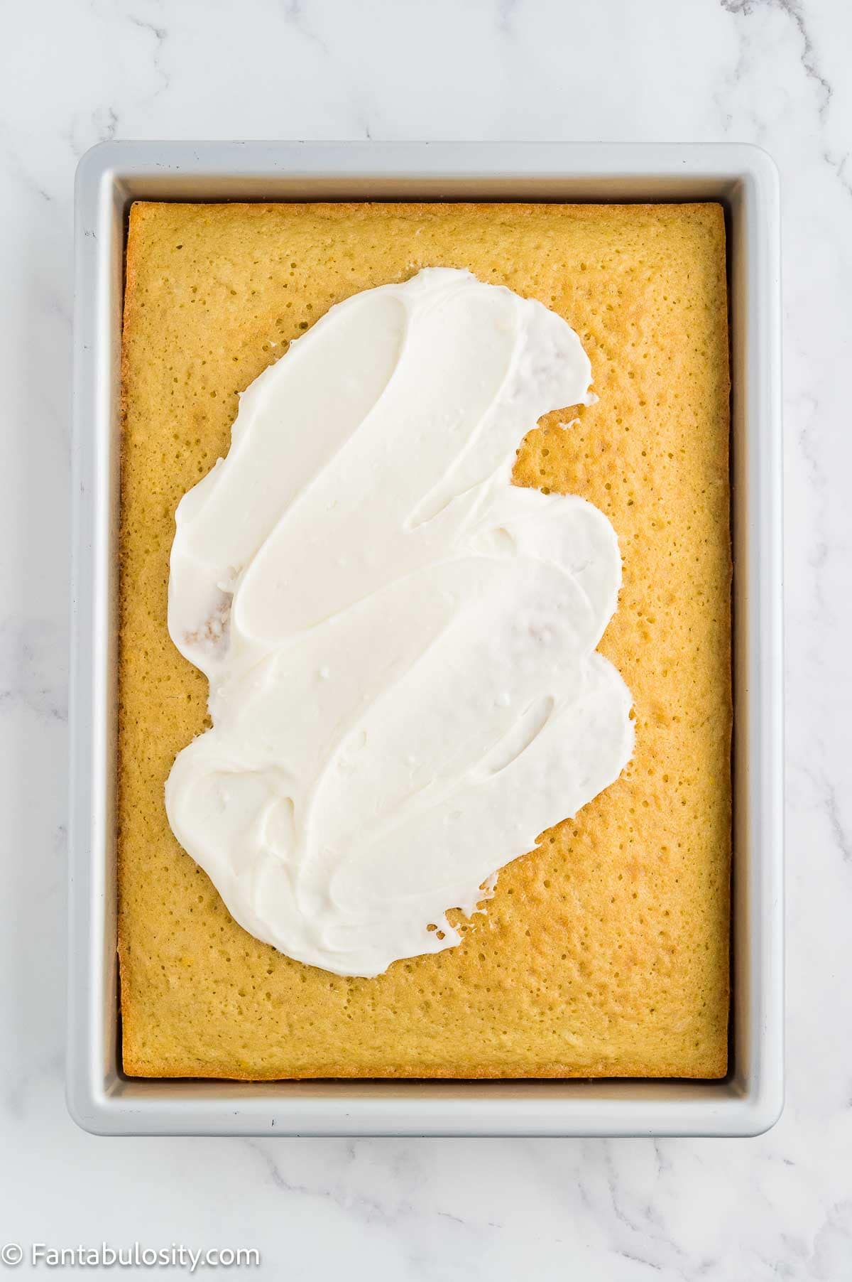 Coconut frosting being spread over the cooled coconut sheet cake in the pan.
