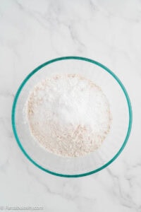Flour, baking powder, salt, and sugar whisked together in a glass mixing bowl.
