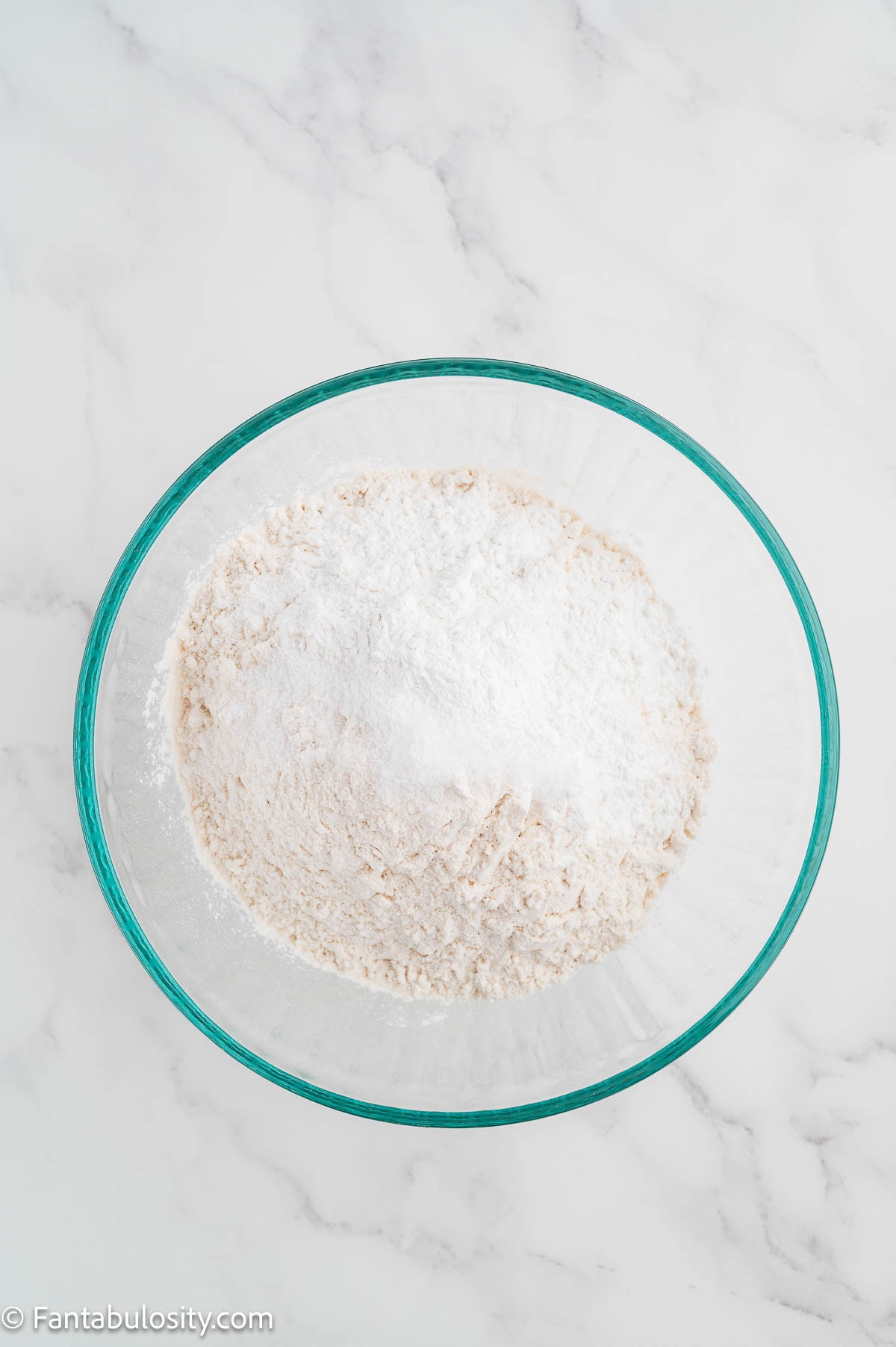 Flour, baking powder, salt, and sugar whisked together in a glass mixing bowl.