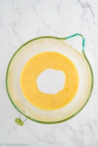 Coconut milk poured into the cake batter in a mixing bowl.