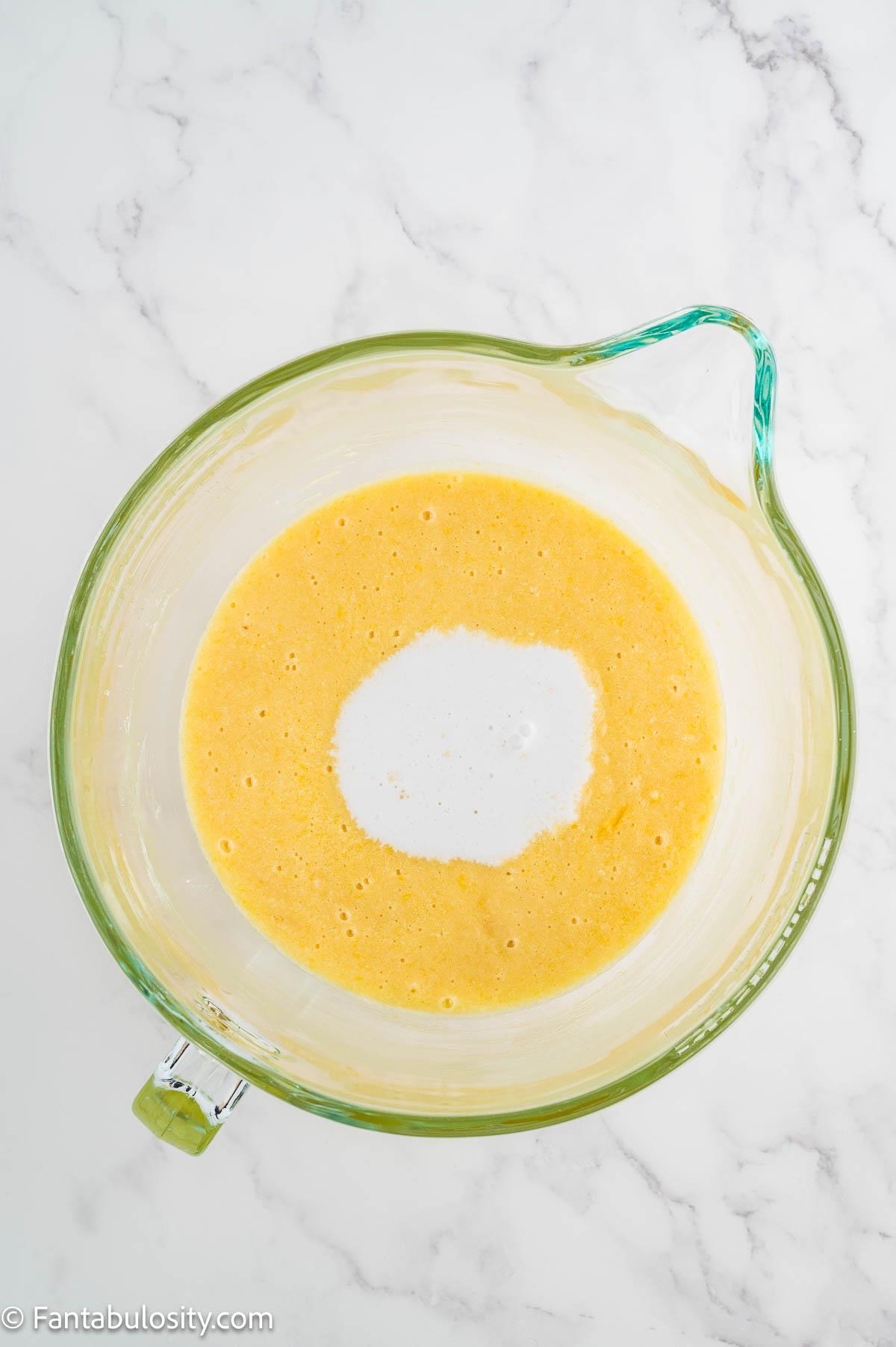 Coconut milk poured into the cake batter in a mixing bowl.