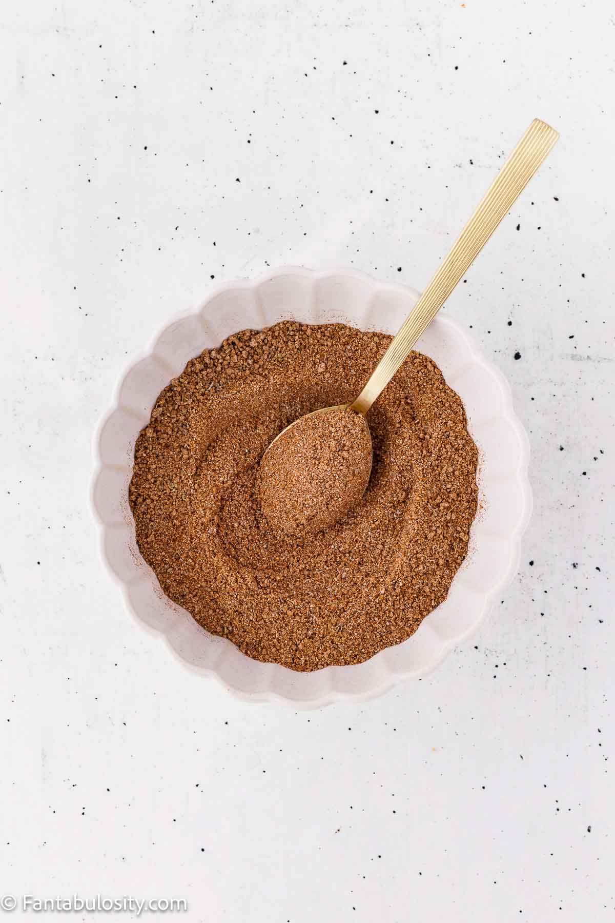 Homemade dry rub for ribs mixed in a white bowl with a wooden spoon